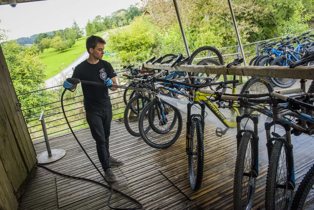 Man washing a bike with a powerful hose on a wooden deck