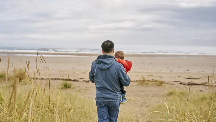 Rear view of man carrying small boy as they walk out to sea shore, Tentsmuir beach , near Leuchars