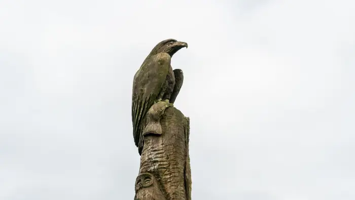  A wooden totem pole with an eagle holding a fish with an owl under it.
