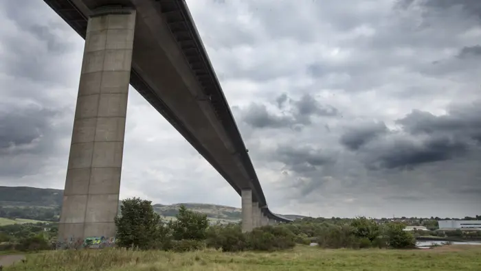The underside of a bridge going over a meadow and trees, with a town in the background