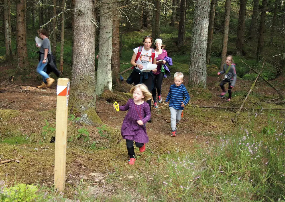 Two women follow a young girl and boy towards an orienteering marker post 