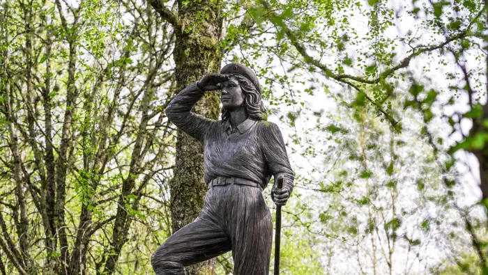 Statue of a lumberjill surrounded by trees.