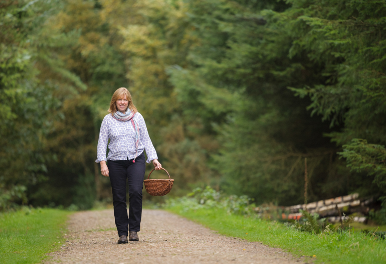 Woman walking on woodland path with wicker basket in hand, Denlethen, near Laurencekirk, Aberdeenshire