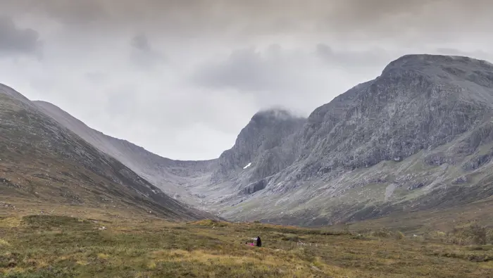 People walking in a grass covered valley near the top of a mountain