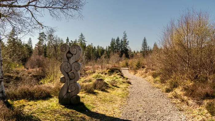Path through a woodland with a sculpture on the left hand side.