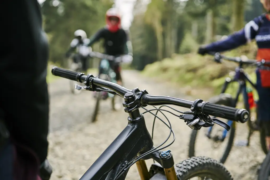 Detail of handlebars and front tyre of black mountain bike with cyclist (mostly unseen) sitting in the saddle, on stony track in Glentress Forest, near Peebles