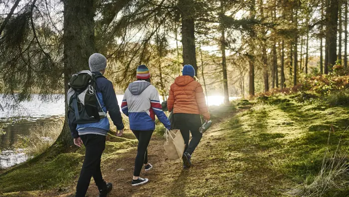 Three people walking along a path with sunlight coming through the trees.