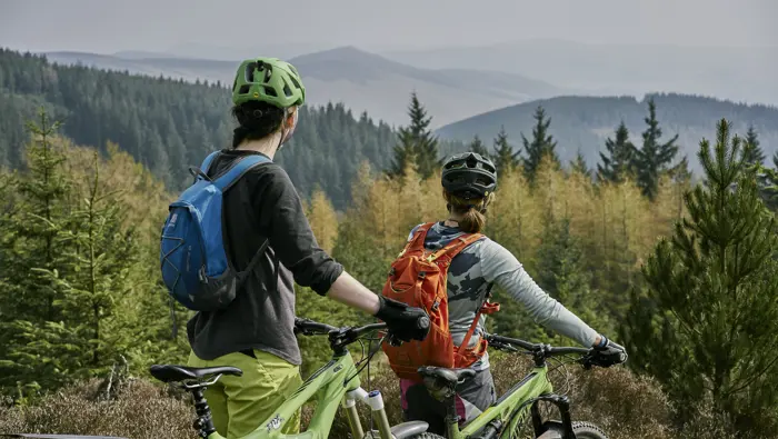Two people with bikes looking out to a forest from a high viewpoint.