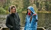 A man and woman in thick waterproof coats stand at the loch side
