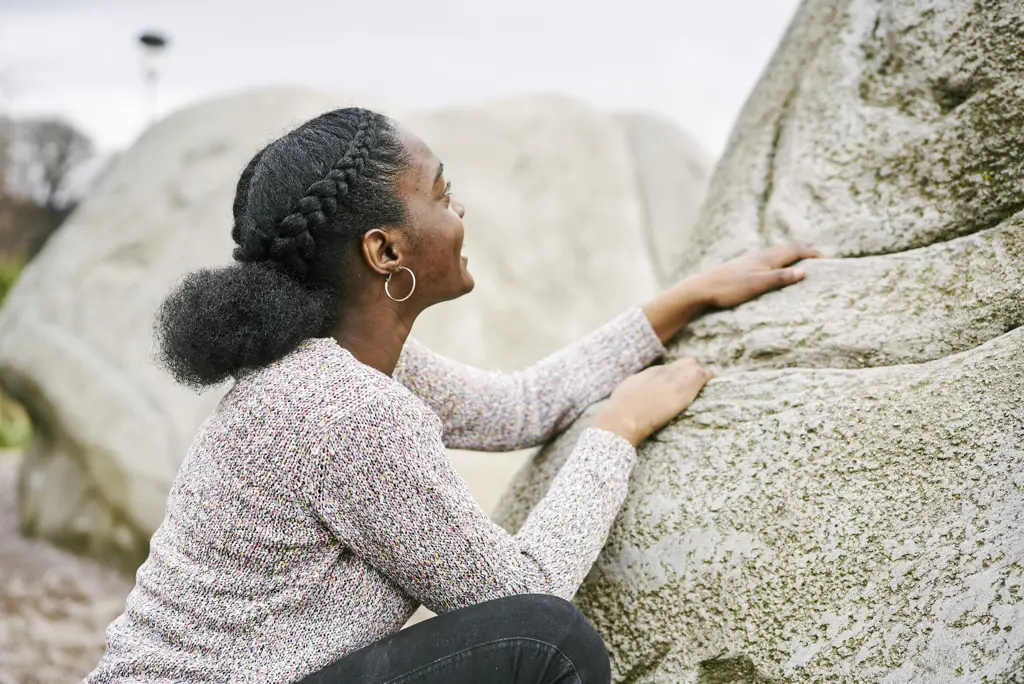 Young girl in grey jumper climbing up boulder at Cuningar Loop Woodland Park, Glasgow