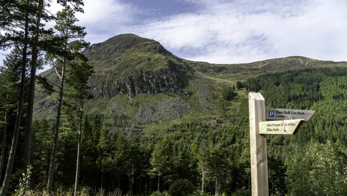 A wooden directional sign in front of a hill