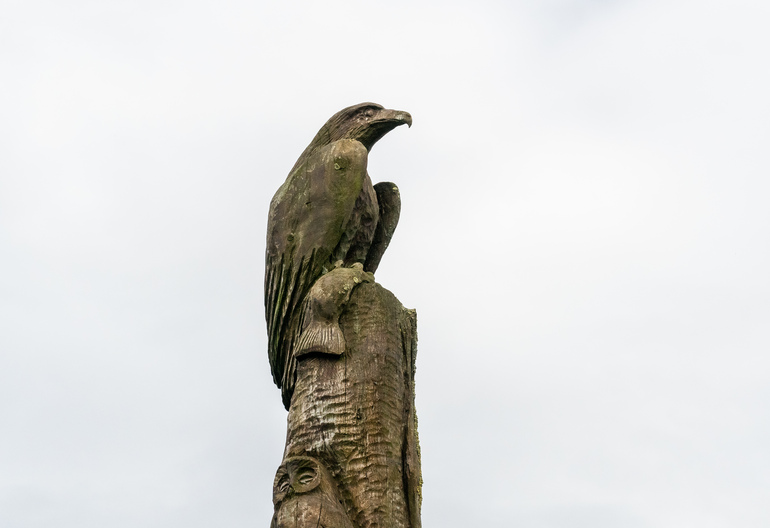 A wooden totem pole with an eagle holding a fish with an owl under it.