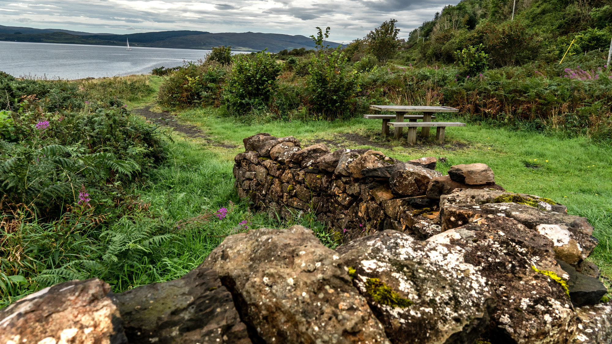 A wooden picnic bend next to the sea with a stone wall