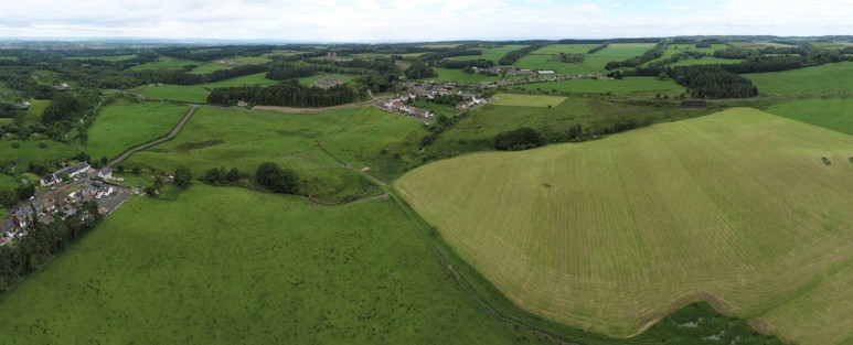 An aerial image of green fields with trees and two groups of buildings visible in the distance.