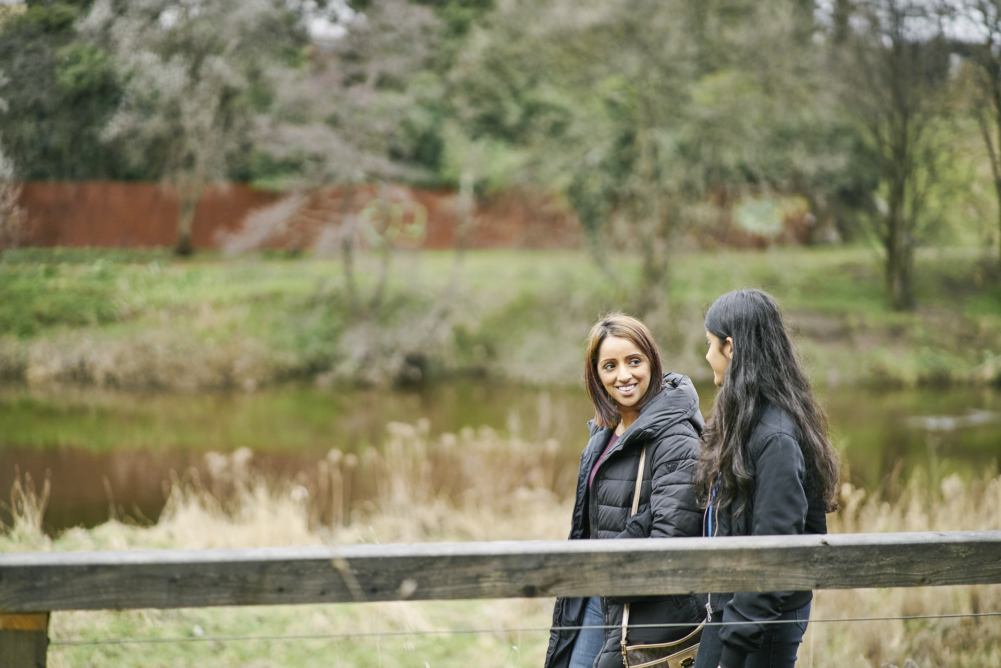 Young woman and teenage girl stroll along wooden boardwalk beside River Clyde at Cuningar Loop Woodland Park, Glasgow