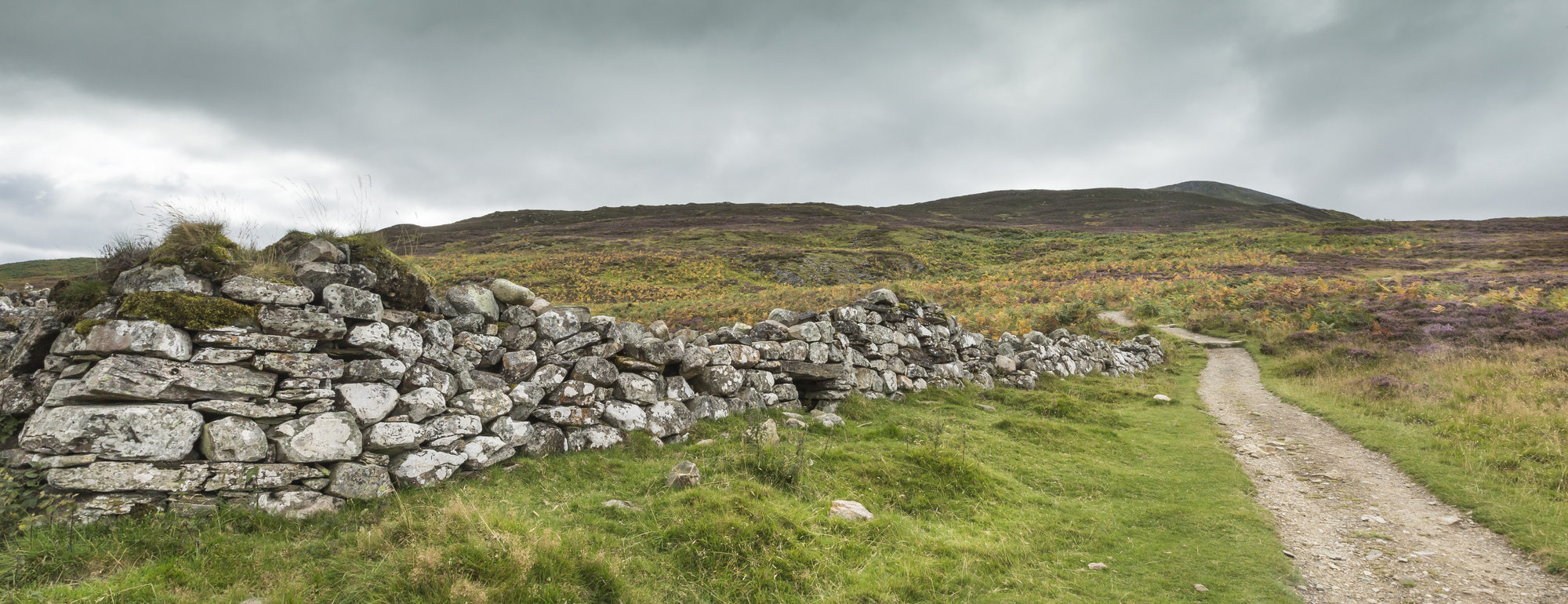 A stone wall at Braes of Foss and Schiehallion with a path alongside it.