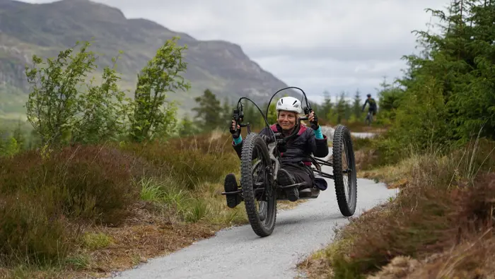 Rider on an adaptive bike with a rider on a mountain bike in the background.