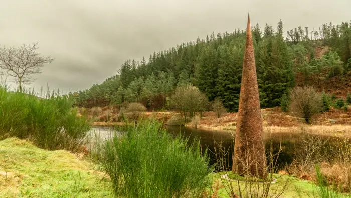 Tall pointed sculpture next to a loch.