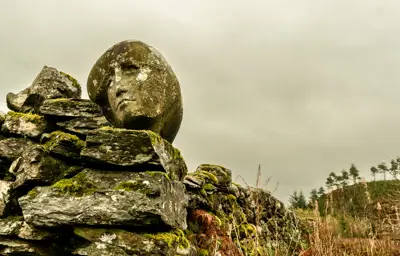 A women's head carved into a stone wall with trees and long grass