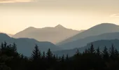 Silhouettes of distant hills, mountains and conifer forest beneath a sunny and cloudy evening sky from Blackmuir Wood
