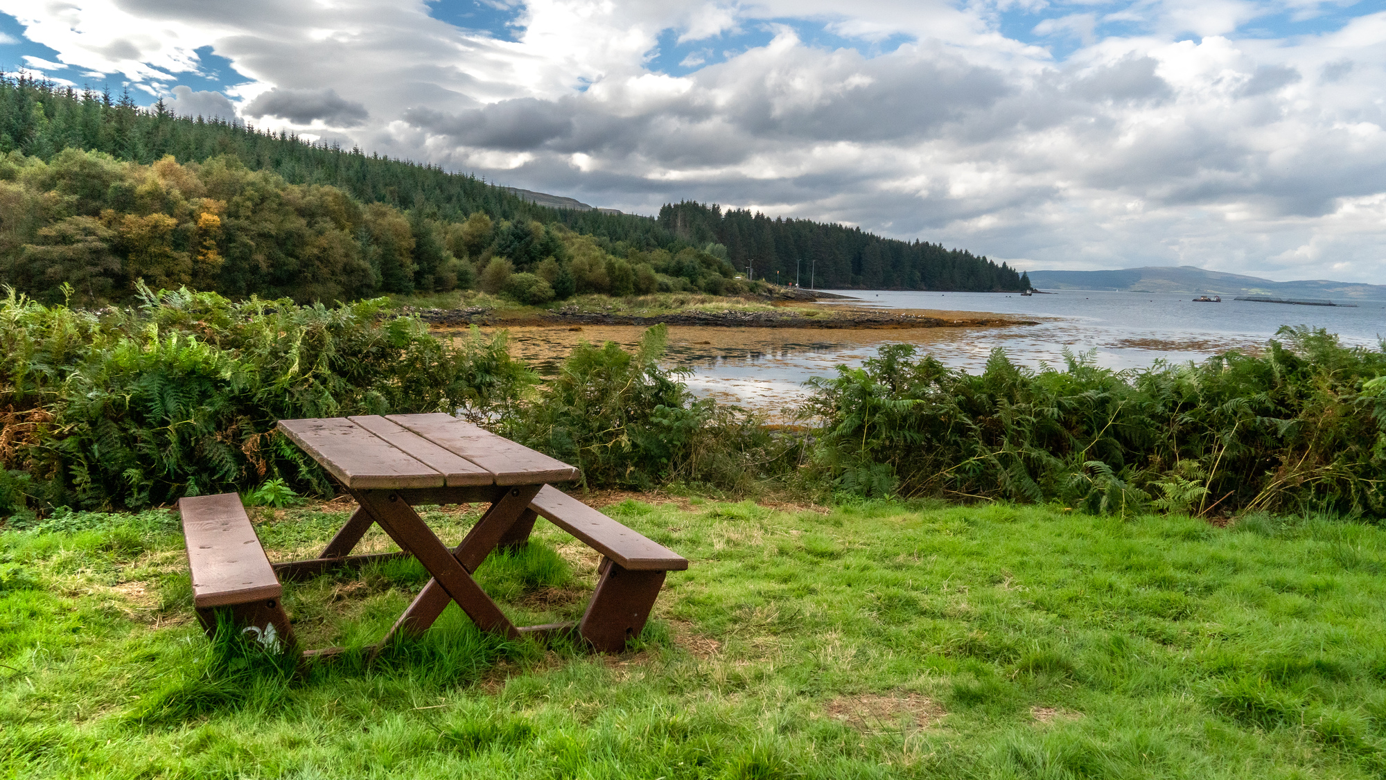  A picnic bench overlooking the shoreline and sea with islands in the background