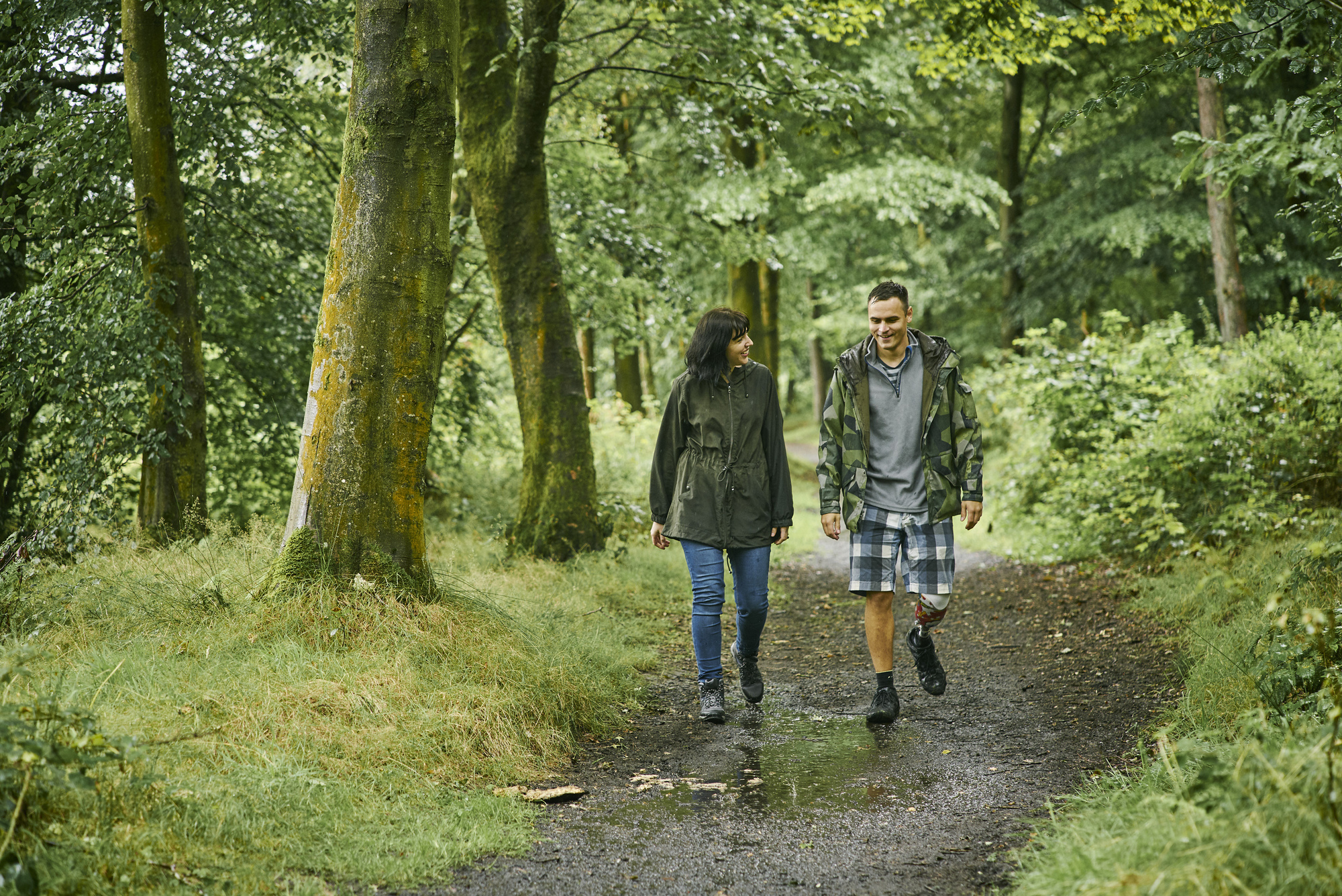 Woman and man with prosthetic leg walk through woodland, Larbert Woods in grounds of Forth Valley Royal Hospital, Larbert
